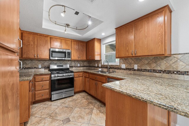 kitchen featuring a sink, appliances with stainless steel finishes, brown cabinetry, and a tray ceiling