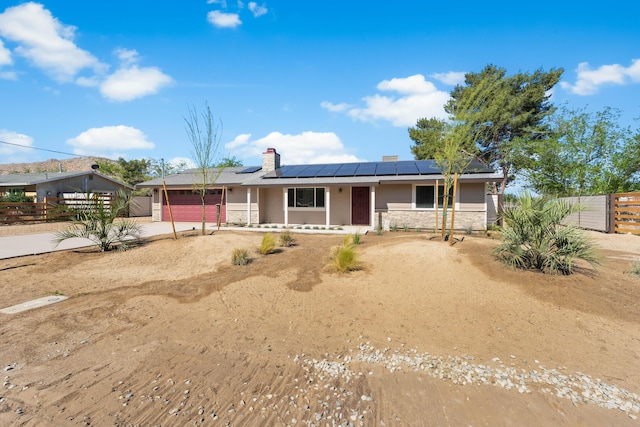 single story home featuring a garage, fence, covered porch, roof mounted solar panels, and driveway