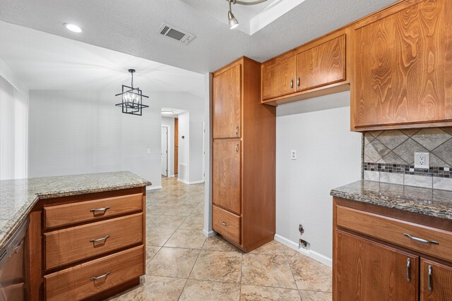 kitchen featuring visible vents, decorative backsplash, brown cabinets, dark stone countertops, and hanging light fixtures
