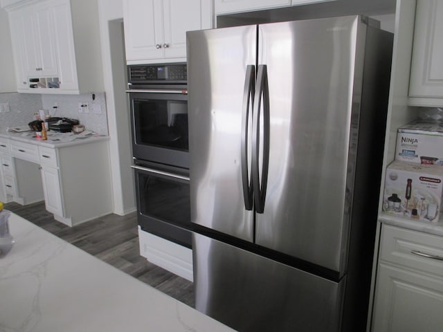 kitchen with freestanding refrigerator, double wall oven, light wood-type flooring, white cabinetry, and backsplash