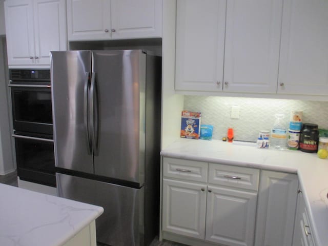 kitchen with dobule oven black, white cabinetry, decorative backsplash, and freestanding refrigerator