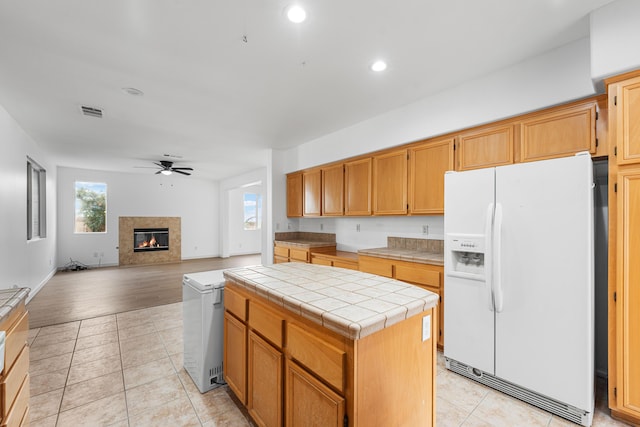 kitchen featuring ceiling fan, tile counters, a center island, white refrigerator with ice dispenser, and light tile patterned floors