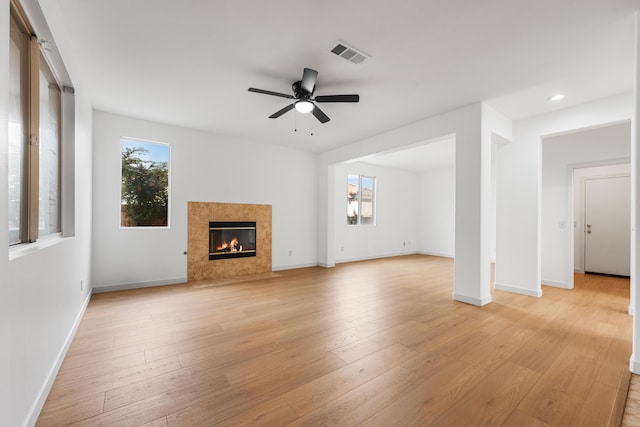 unfurnished living room featuring ceiling fan, light hardwood / wood-style flooring, a high end fireplace, and plenty of natural light