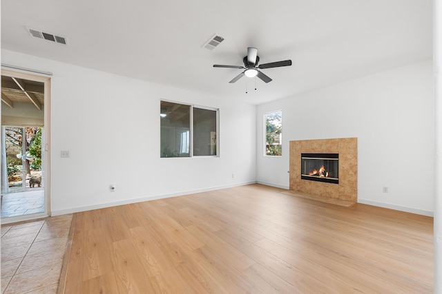 unfurnished living room featuring ceiling fan, light wood-type flooring, and a tiled fireplace