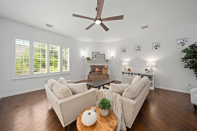 living room featuring a glass covered fireplace, visible vents, baseboards, and dark wood finished floors