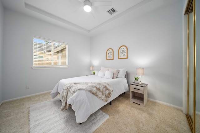 carpeted bedroom with a tray ceiling, baseboards, visible vents, and a closet