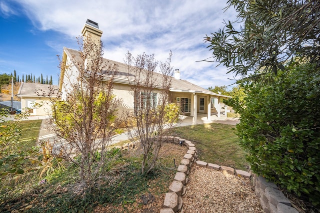 back of house featuring stucco siding, a chimney, and a patio