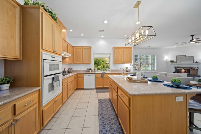 kitchen with a sink, under cabinet range hood, open floor plan, white appliances, and light tile patterned flooring