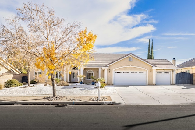 view of front facade featuring concrete driveway, a tile roof, stucco siding, an attached garage, and a gate