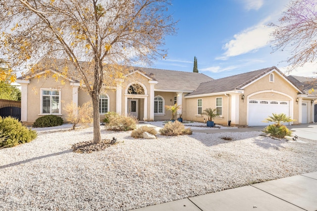 view of front of property featuring stucco siding, driveway, a tile roof, fence, and a garage