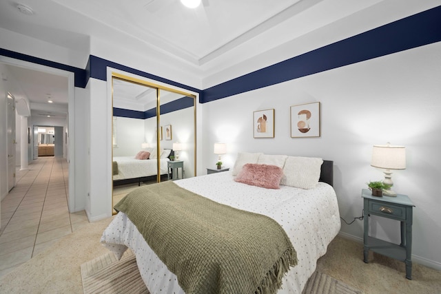 bedroom featuring baseboards, light tile patterned floors, light carpet, a closet, and a raised ceiling