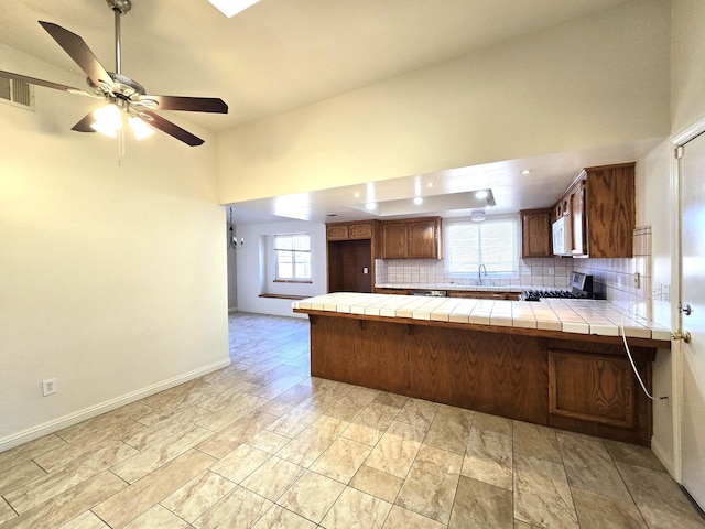 kitchen featuring tile countertops, tasteful backsplash, stainless steel range, ceiling fan, and kitchen peninsula