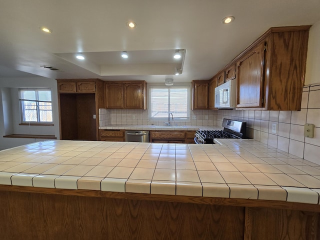 kitchen featuring appliances with stainless steel finishes, tile countertops, tasteful backsplash, sink, and a tray ceiling