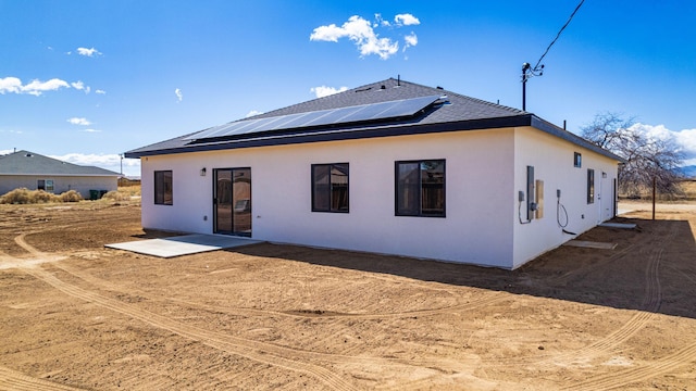 rear view of property featuring stucco siding, roof mounted solar panels, and a shingled roof