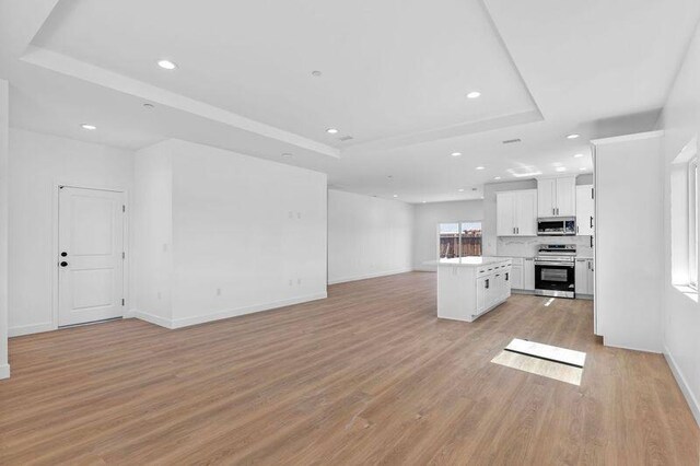 kitchen featuring a tray ceiling, open floor plan, white cabinetry, stainless steel appliances, and light wood-style floors