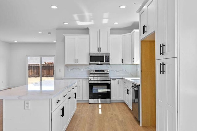 kitchen with backsplash, white cabinetry, stainless steel appliances, and light wood-style floors
