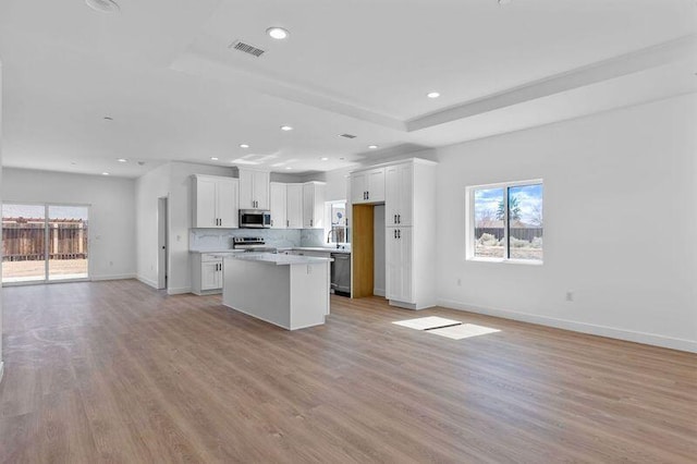 kitchen with a tray ceiling, stainless steel appliances, light wood-style floors, and open floor plan