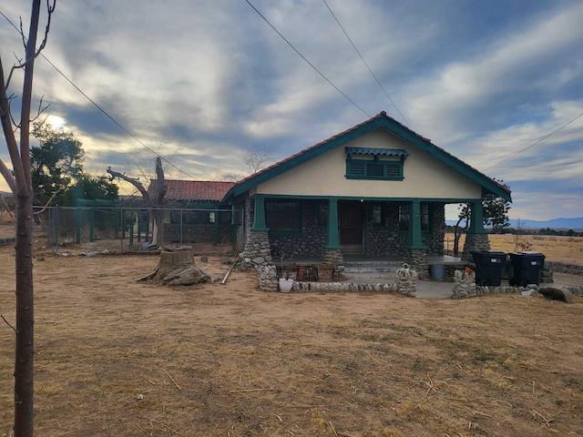 view of front facade featuring stone siding, covered porch, fence, and stucco siding