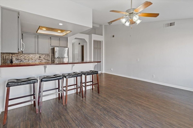 kitchen with a breakfast bar area, tasteful backsplash, appliances with stainless steel finishes, dark hardwood / wood-style floors, and gray cabinets