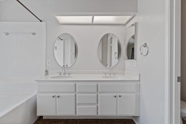 bathroom featuring tiled tub, vanity, and toilet