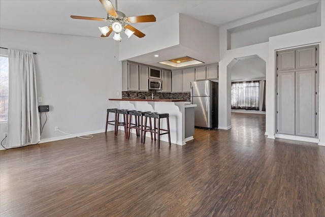 kitchen featuring gray cabinetry, dark hardwood / wood-style flooring, a kitchen breakfast bar, kitchen peninsula, and stainless steel appliances