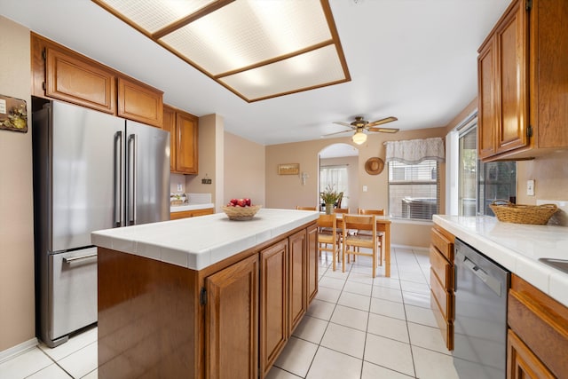 kitchen with appliances with stainless steel finishes, ceiling fan, light tile patterned floors, a center island, and tile counters