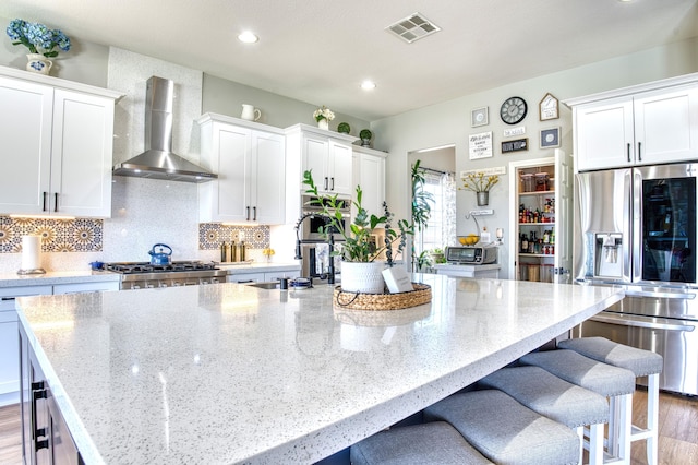 5549 Bobbie Ave, Palmdale, CA 93551 - kitchen with stainless steel fridge, wall chimney range hood, a large island with sink, white cabinets, and light stone counters