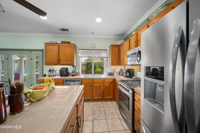 43432 Bale Ct, Lancaster, CA 93535 - kitchen featuring stainless steel appliances, tile counters, brown cabinetry, ornamental molding, and recessed lighting