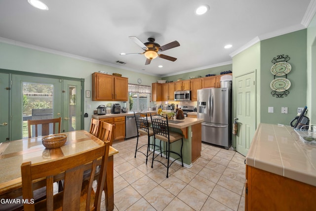 43432 Bale Ct, Lancaster, CA 93535 - kitchen featuring appliances with stainless steel finishes, tile countertops, a breakfast bar area, a ceiling fan, and crown molding