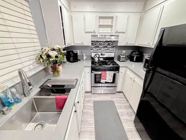 kitchen with exhaust hood, black refrigerator, gas stove, white cabinetry, and sink