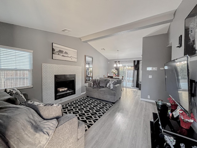 living room with a tile fireplace, vaulted ceiling with beams, a chandelier, and hardwood / wood-style floors