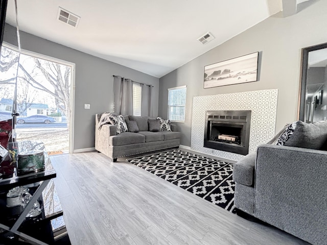 living room featuring lofted ceiling, wood-type flooring, and a tile fireplace