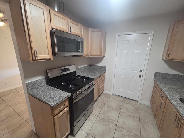 kitchen with stainless steel appliances, light brown cabinetry, light tile patterned flooring, and baseboards