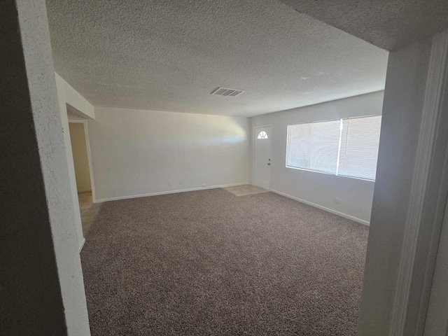 carpeted spare room featuring a textured ceiling and baseboards