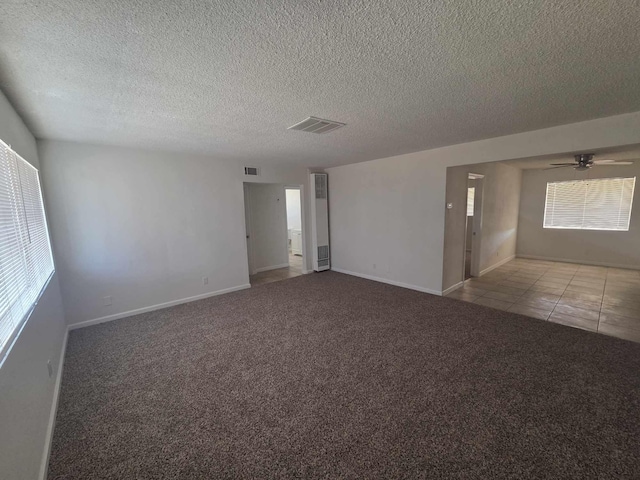 carpeted empty room with a textured ceiling, ceiling fan, baseboards, and tile patterned flooring
