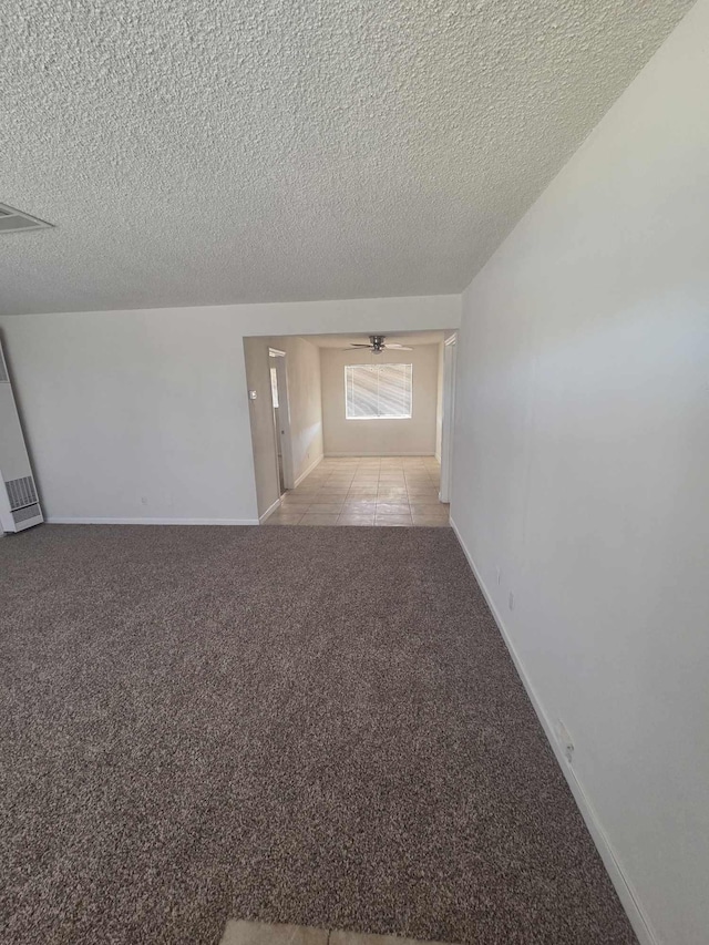 empty room featuring carpet flooring, a textured ceiling, baseboards, and tile patterned flooring