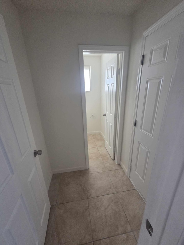 hall featuring light tile patterned floors and baseboards
