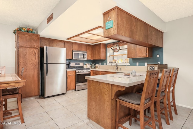 1037 Herzel Ave, Lancaster, CA 93535 - kitchen with appliances with stainless steel finishes, a peninsula, a textured ceiling, light countertops, and light tile patterned floors