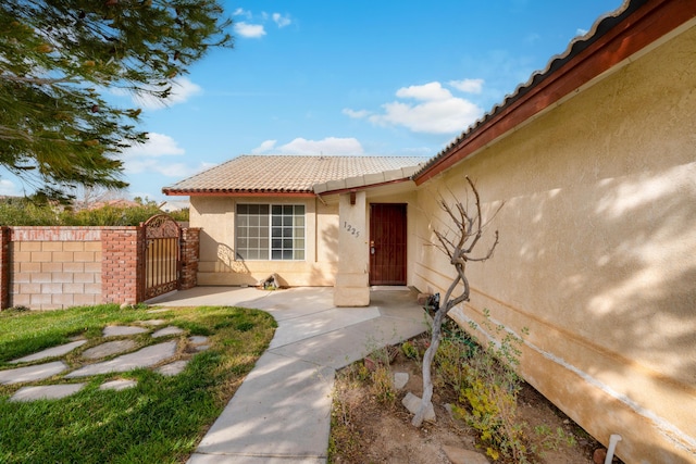 doorway to property featuring stucco siding, a tiled roof, fence, and a gate