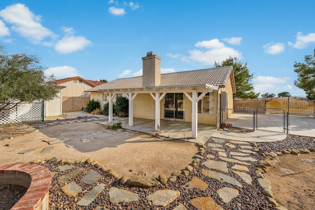 rear view of property featuring fence, a tile roof, a chimney, a patio area, and a gate