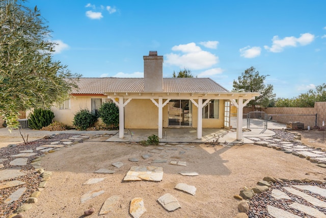 rear view of property with fence, a tile roof, stucco siding, a chimney, and a patio area