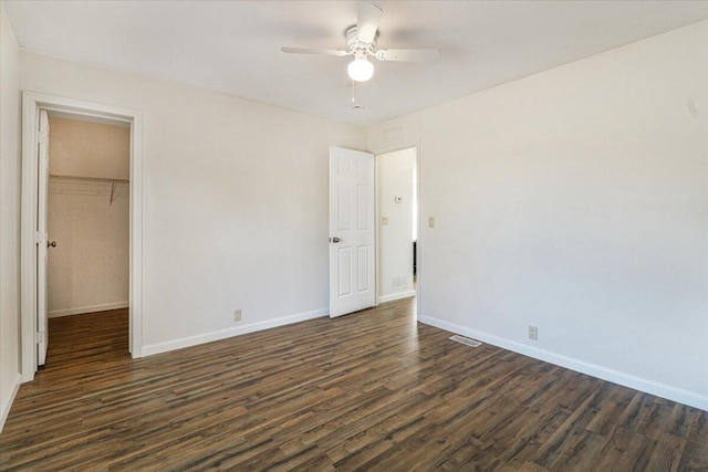 unfurnished bedroom with ceiling fan, dark hardwood / wood-style flooring, a walk in closet, and a closet