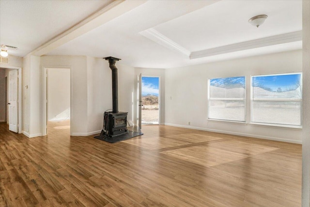 unfurnished living room featuring hardwood / wood-style flooring, a raised ceiling, and a wood stove