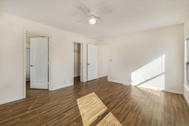 unfurnished bedroom featuring a closet, dark hardwood / wood-style floors, a spacious closet, and ceiling fan