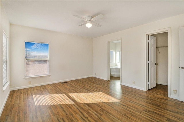 unfurnished bedroom featuring ensuite bath, ceiling fan, dark hardwood / wood-style flooring, a walk in closet, and a closet