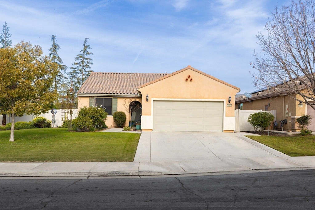 mediterranean / spanish-style house featuring an attached garage, fence, a tiled roof, stucco siding, and a front lawn