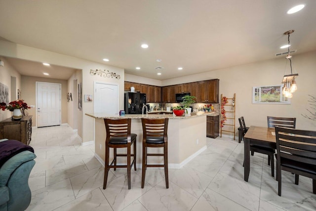 kitchen with backsplash, black appliances, light stone countertops, an island with sink, and decorative light fixtures