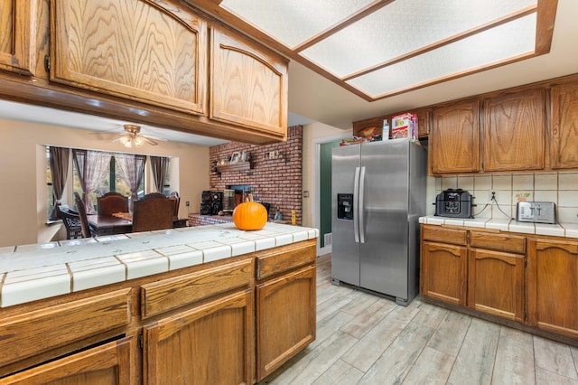 kitchen featuring tile countertops, light hardwood / wood-style flooring, ceiling fan, tasteful backsplash, and stainless steel fridge with ice dispenser