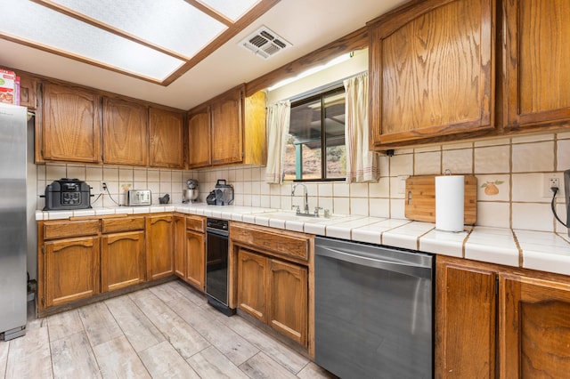 kitchen with appliances with stainless steel finishes, backsplash, tile countertops, and light hardwood / wood-style flooring