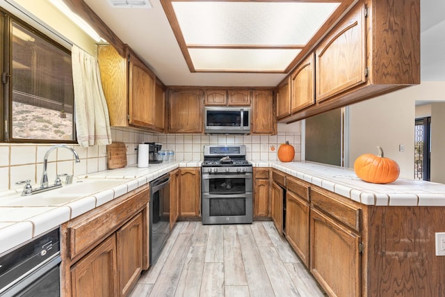 kitchen with sink, decorative backsplash, tile counters, kitchen peninsula, and stainless steel appliances